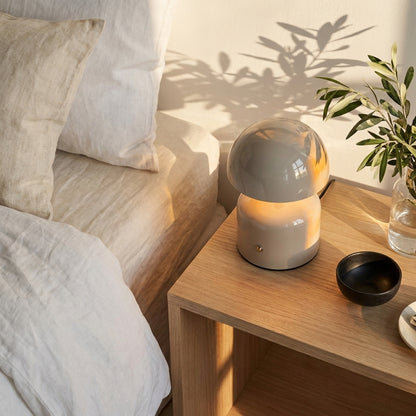 Vista flat lay de um candeeiro de mesa cinzento sobre uma mesa de apoio de madeira clara num ambiente de quarto, com rou