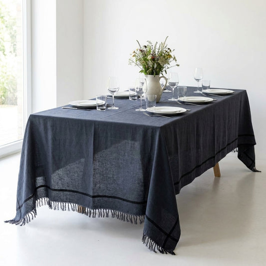 Toalha de mesa Toscana em linho cinzento escuro com risca preta e franjas, numa mesa posta para seis