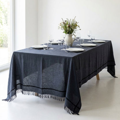 Toalha de mesa Toscana em linho cinzento escuro com risca preta e franjas, numa mesa posta para seis