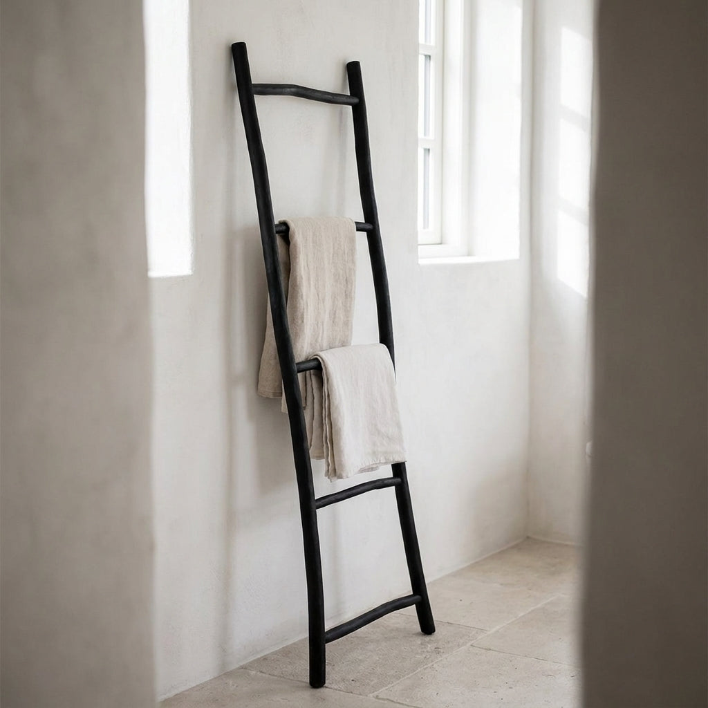 Escada decorativa Tulum em teca preta encostada a uma parede de casa de banho, com toalhas de linho nas travessas