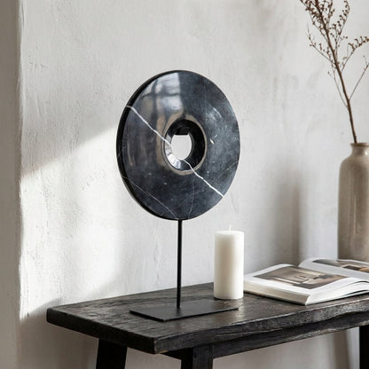 Disco decorativo em marmore preto com suporte de metal, numa consola de madeira escura com parede caiada