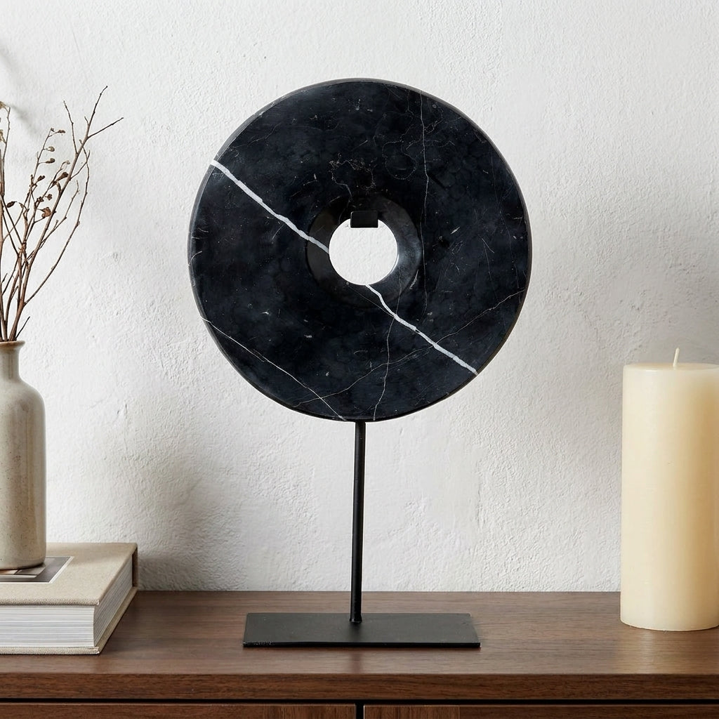 Disco decorativo em marmore preto com suporte de metal, numa consola de madeira escura com parede caiada, livro e vela
