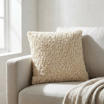 Almofada Tossa em boucle cru no canto de um sofa de linho claro, com luz natural lateral