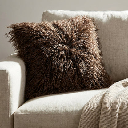 Almofada Zaria de pelo comprido castanho num sofa claro em linho cru, com luz rasante nos fios