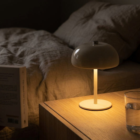 Candeeiro Margate bege recarregavel aceso numa mesa-de-cabeceira, ao lado de uma cama de linho