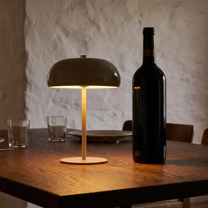 Candeeiro Margate taupe recarregavel aceso numa mesa de jantar de madeira escura ao fim do dia