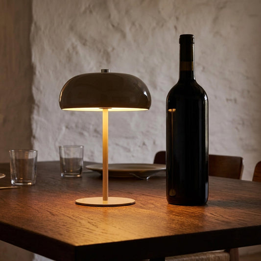 Candeeiro Margate taupe recarregavel aceso numa mesa de jantar de madeira escura ao fim do dia