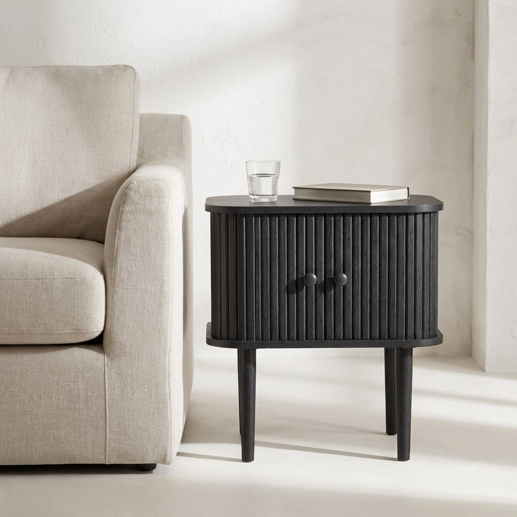 Mesa lateral Nikko preta com portas em ripas curvas, junto a um sofa de linho claro