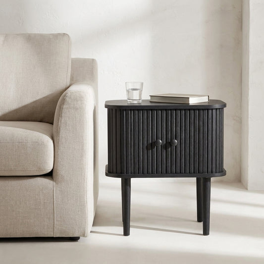 Mesa lateral Nikko preta com portas em ripas curvas, junto a um sofa de linho claro