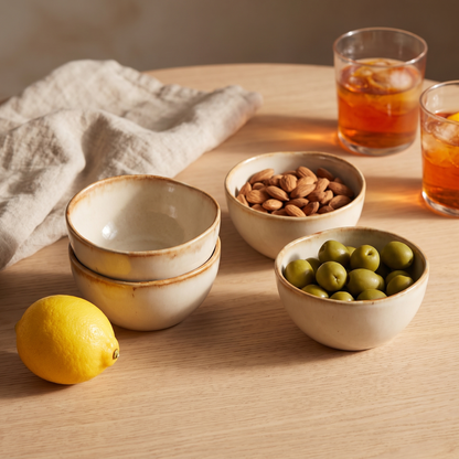 Quatro tigelas pequenas Cascais em gres creme com aro caramelo, numa mesa de aperitivo com amendoas e azeitonas