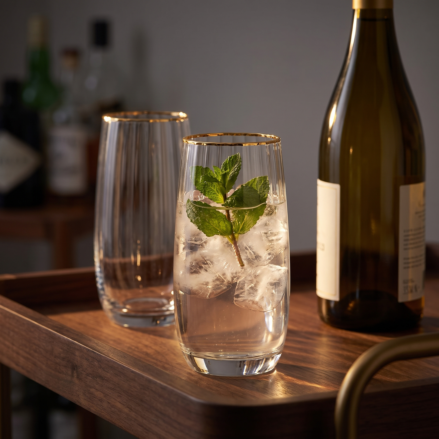 Copos altos com aro dourado em vidro transparente canelado, num carrinho de bar ao entardecer