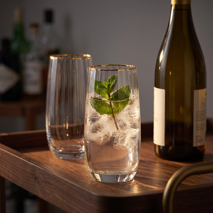 Copos altos com aro dourado em vidro transparente canelado, num carrinho de bar ao entardecer